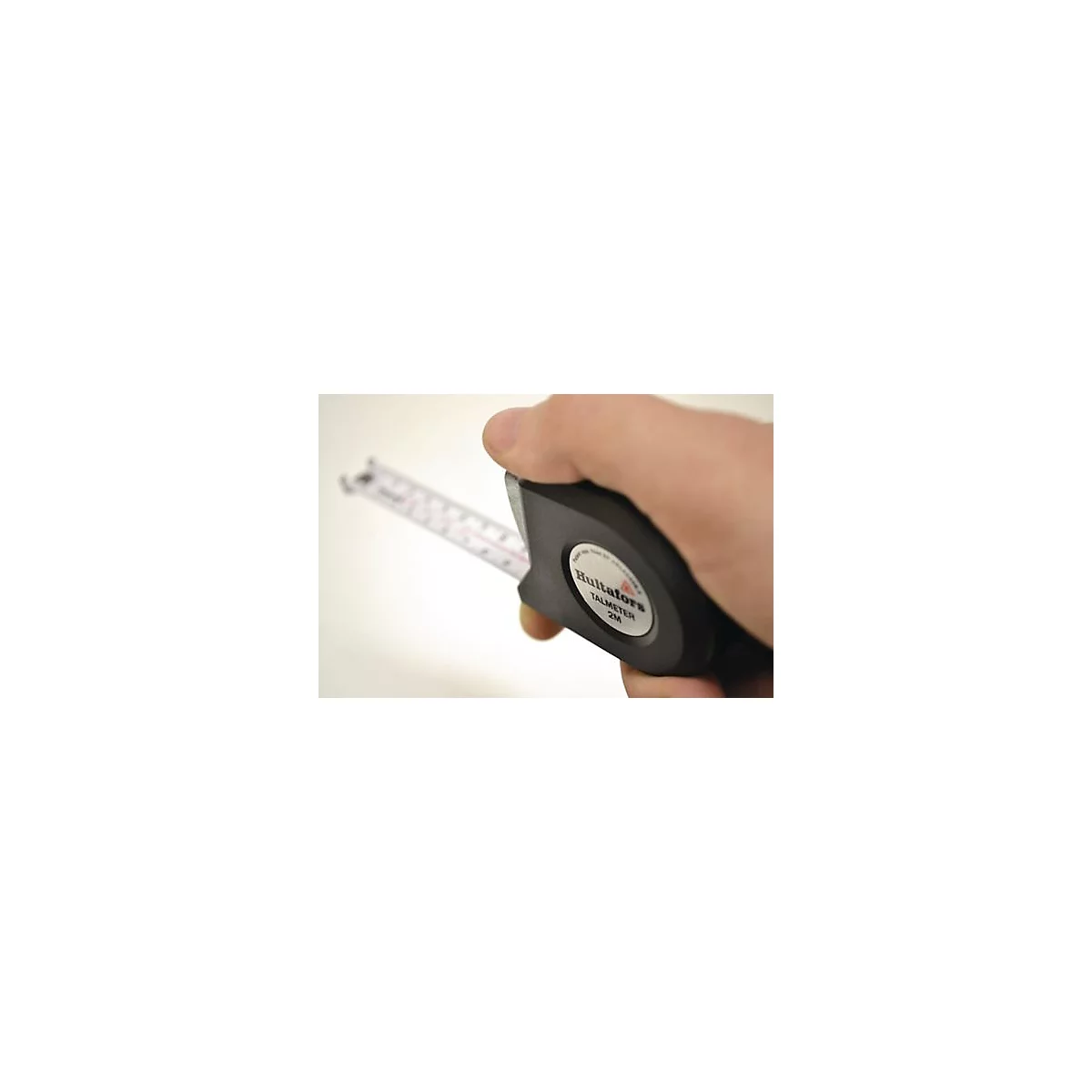 Een hand houdt een zwarte rolmaat vast. Op de rolmaat staat "Hultafors TALMETER 2M".