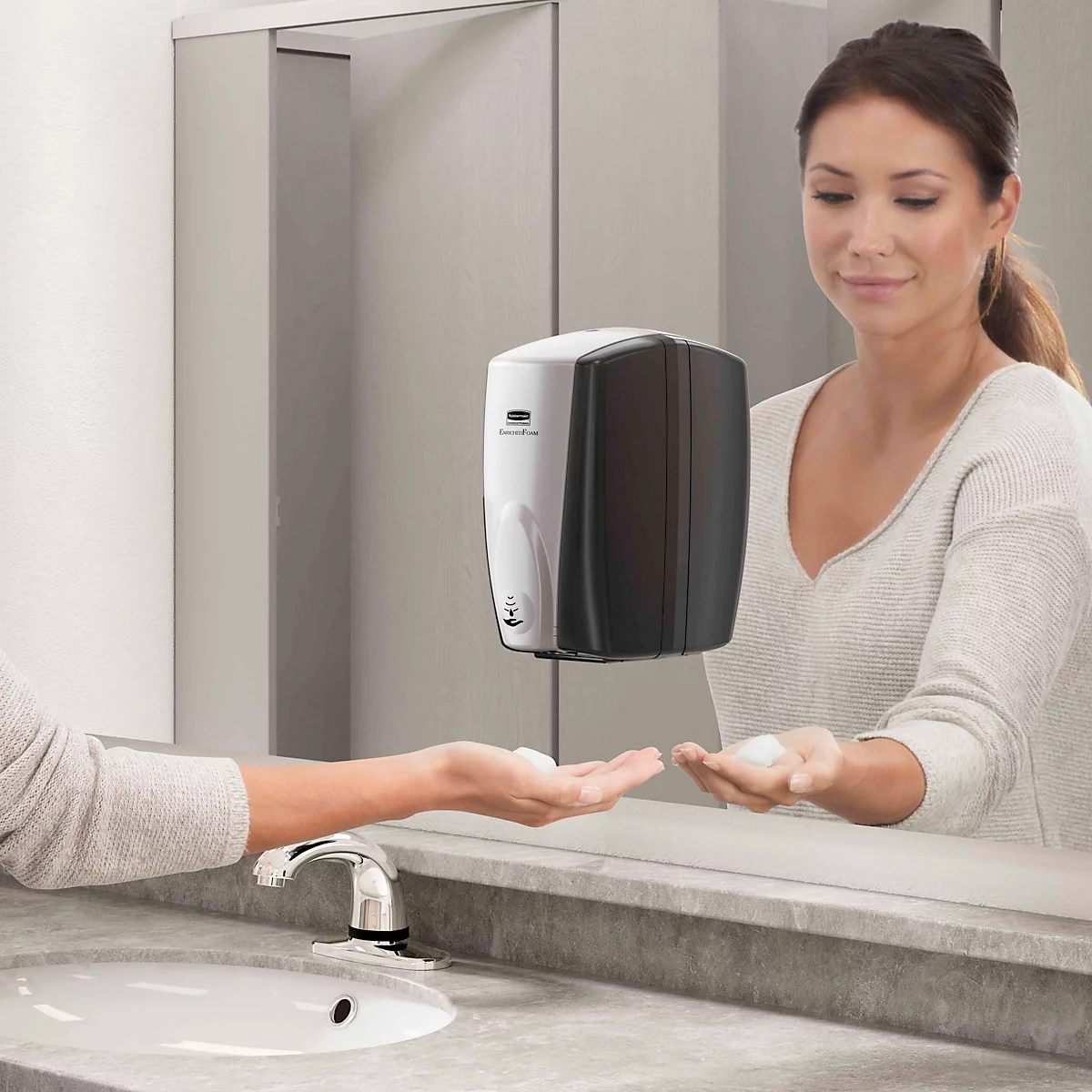 Een vrouw wast haar handen met zeep uit een contactloze zeepdispenser. Ze glimlacht terwijl het schuim in haar handpalm valt.