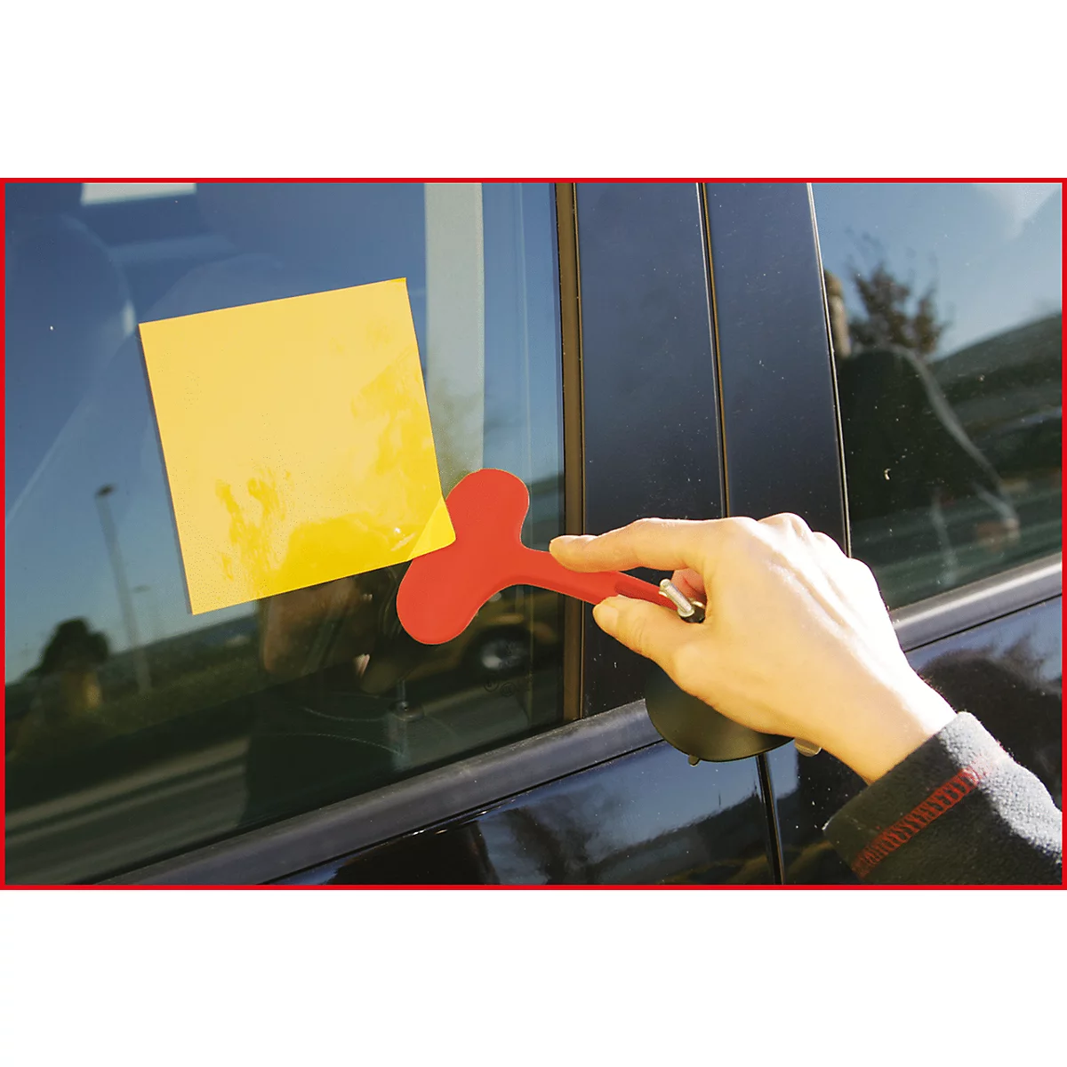 Hand hält roten Saugnapf an Autoscheibe mit gelbem Haftzettel.
