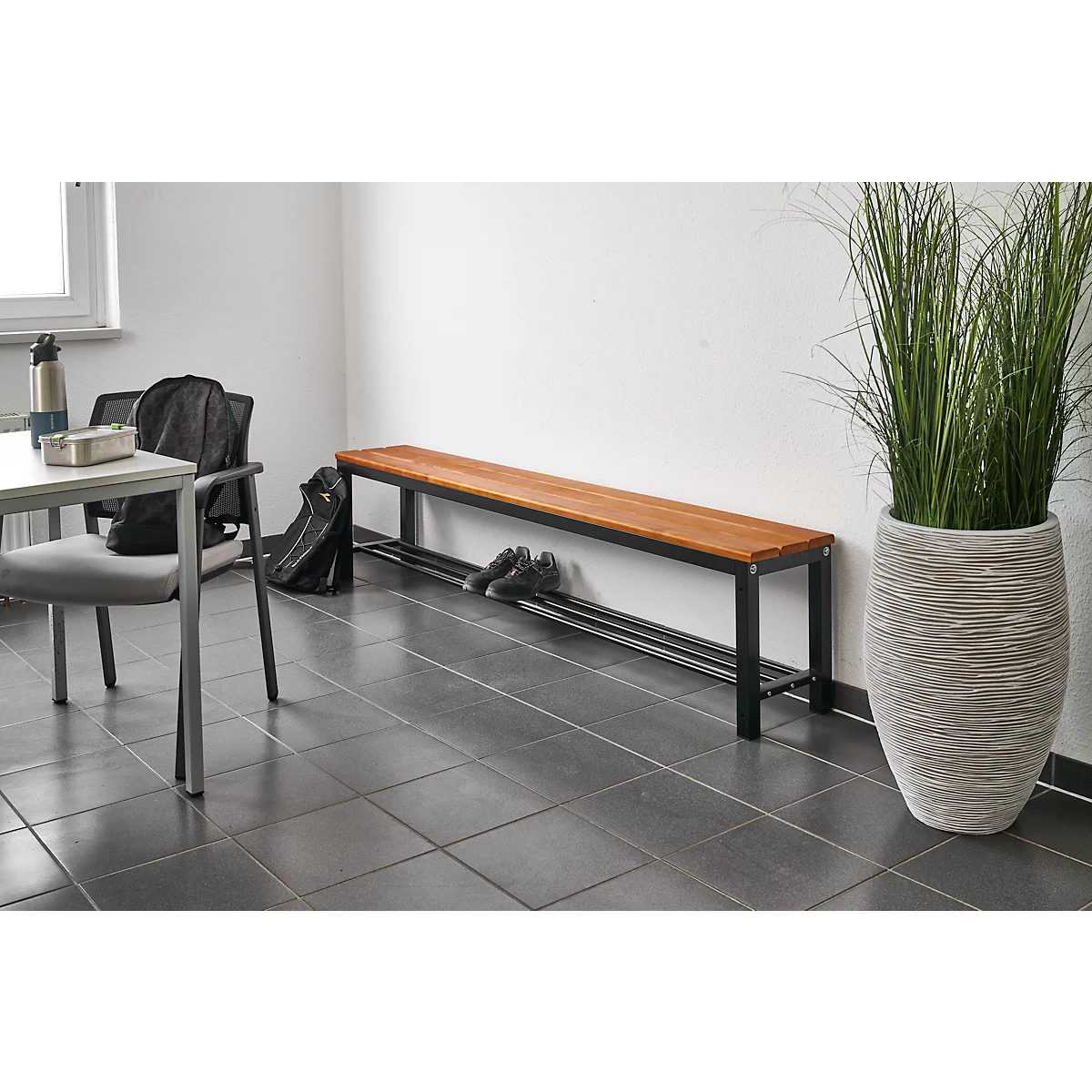 Houten bank met zwart frame en plank. Daarnaast een grote plant in een decoratieve pot.