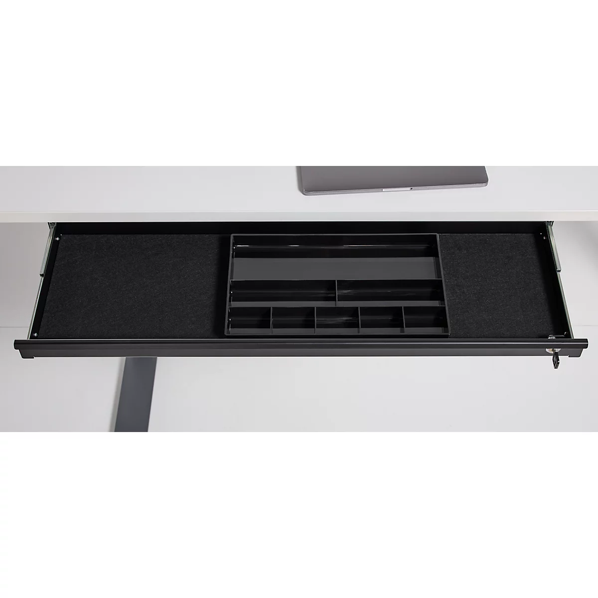 Ausgezogene Schublade unter einem Schreibtisch mit schwarzem Filz und einem schwarzen Organizer.